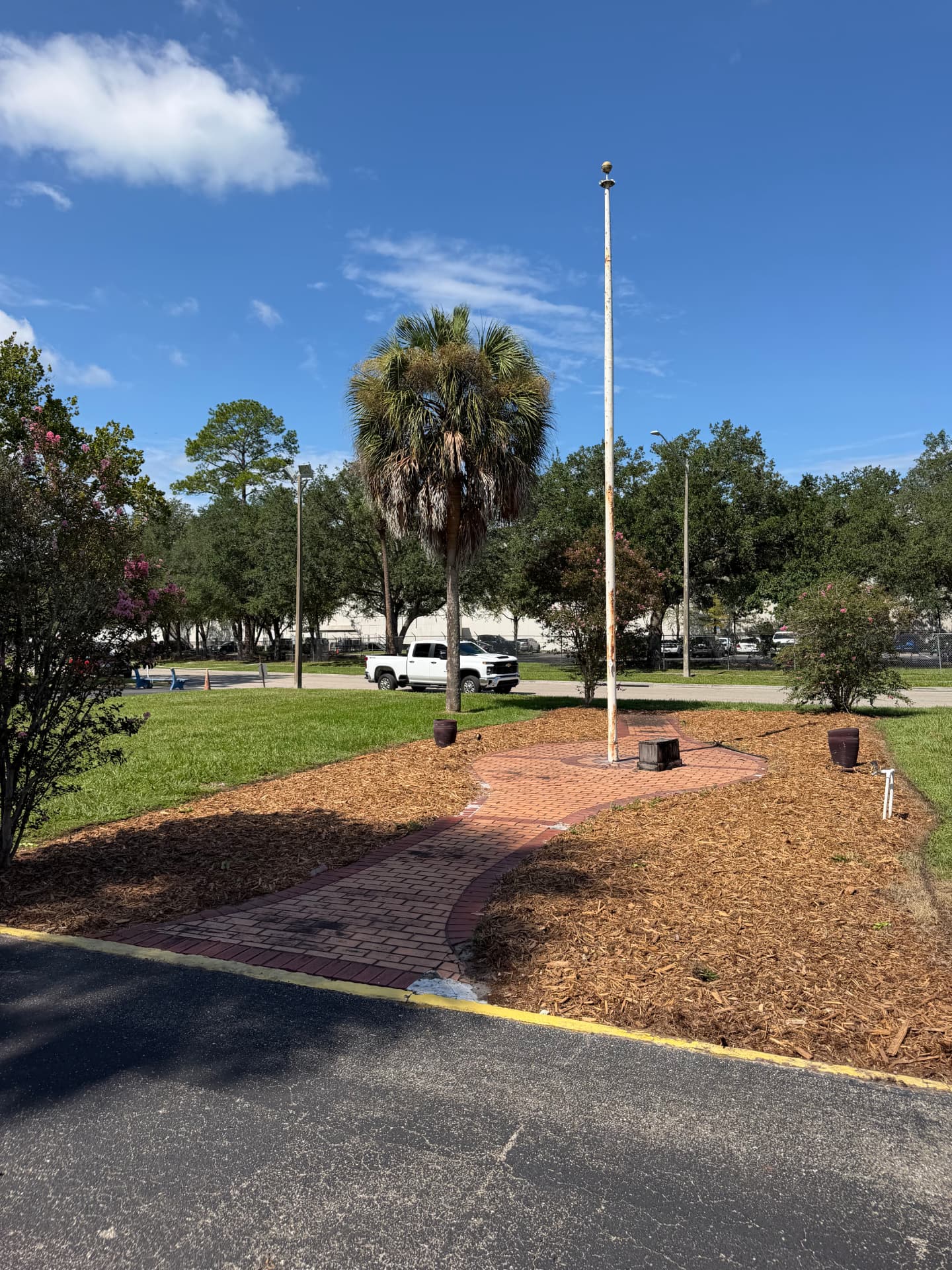 The same flagpole and brick pathway with fresh mulch, defined bed edges, and healthy plantings after service